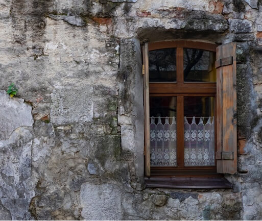 outside of a beautiful old cement building looking at a wooden window frame with lace curtains