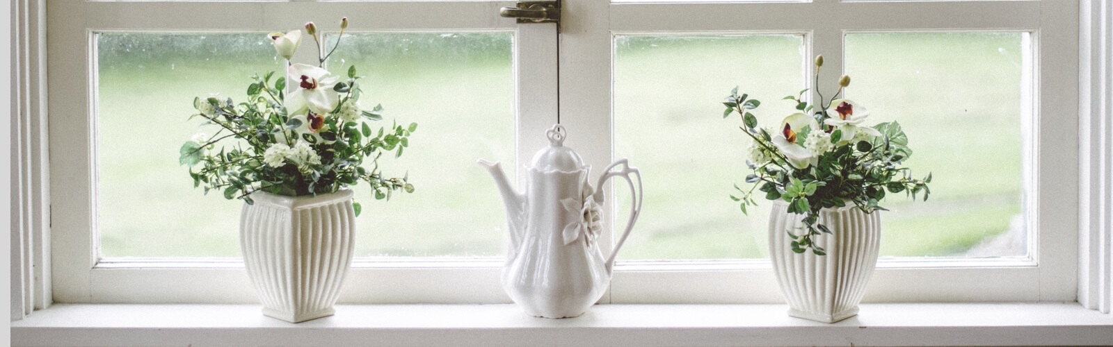 two white vases and a white tea pot on a white window sill overlooking a lawn